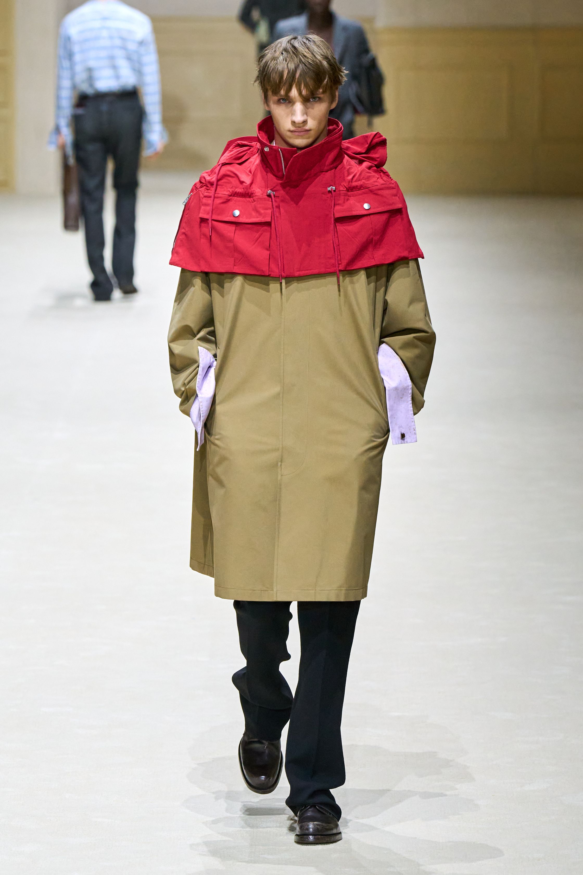 Prada 2026秋冬继续以“制服感”为切入口，重构男性权力与脆弱性的关系。修身西装、直筒大衣与功能性外套在高度理性的廓形中出现，却通过红色针织、围巾与内搭打破秩序。系列在严肃与松动之间反复摇摆，呈现一种当代男性在社会角色与个体情绪之间的张力。这是Prada一贯的冷静叙事，也是其思想性持续领先的关键简-顽石频道趋势研究